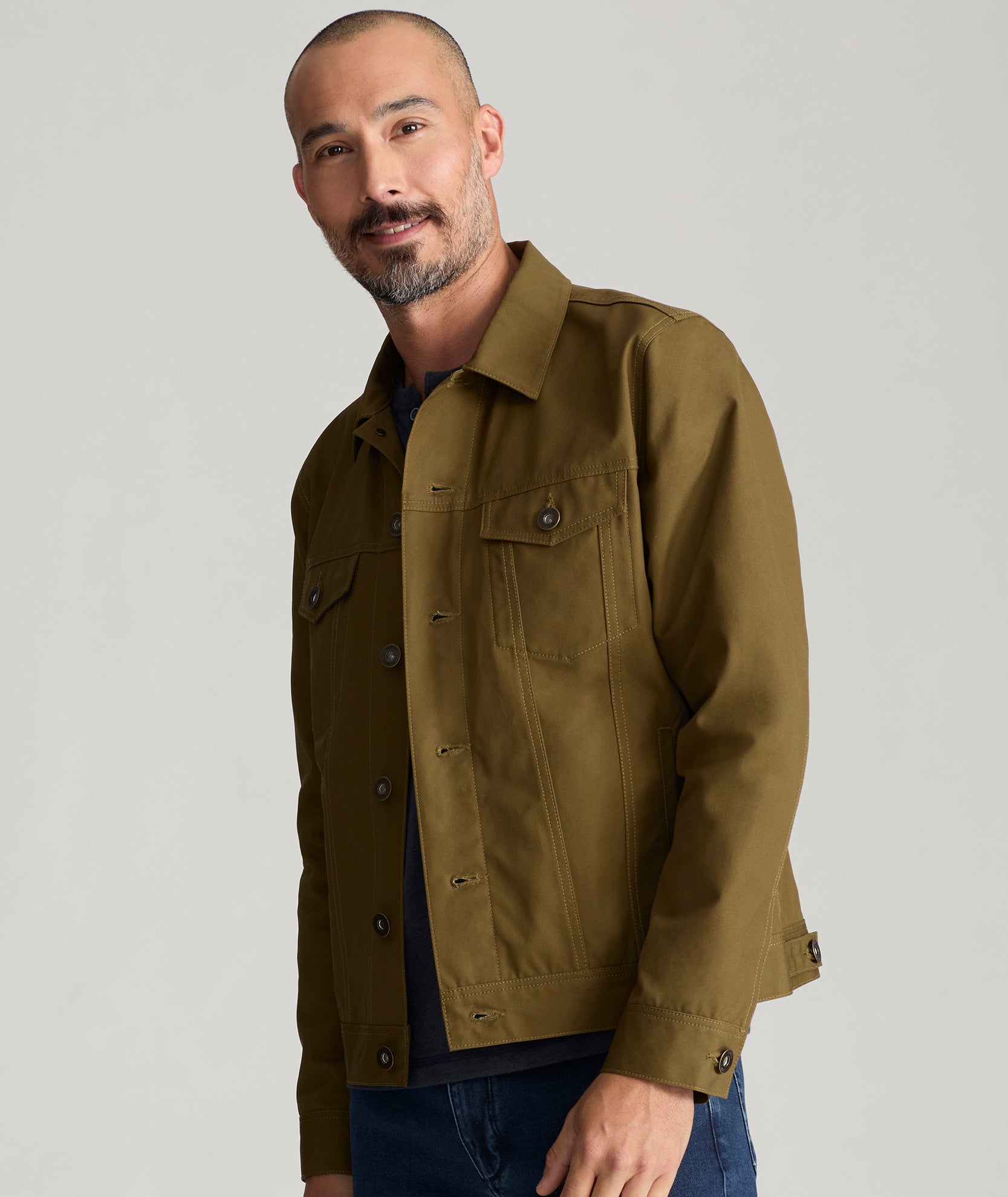 Model is wearing UNTUCKit Rizzo waxed trucker jacket in dark olive. 